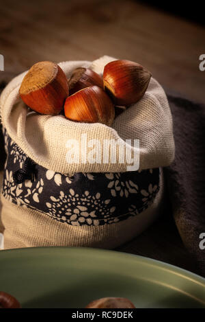 Vertikale Foto von mehreren Haselnüsse. Die Muttern sind mit Muscheln mit brauner Farbe. Die Muttern sind in Leinen Beutel mit weißer Farbe und blauen Streifen platziert. Tasche Stockfoto