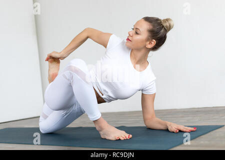 Sportliche junge Frau Yoga Praxis auf weißem Hintergrund zu Hause. Stockfoto
