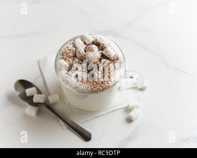 Babyccino - Schlagsahne Milch oder Sahne mit Kakao oder Zimt Pulver und Eibisch. Idee und Rezept für Kinder trinken - warme Sahne Milch, ohne Kaffee. Babyccino in Glas Schale auf Marmortisch. Platz kopieren Stockfoto