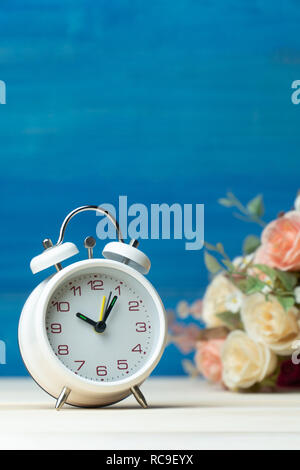 Weiß Wecker und Blumen rosa und rote Rose auf Holztisch und blauer Hintergrund mit Kopie Platz für Text und Inhalt hinzufügen. Stockfoto