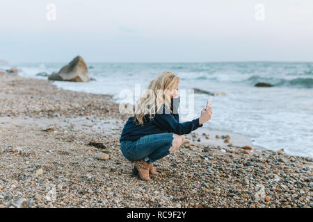 Junge Frau am Strand kauern auf Smartphone, Menemsha, Martha's Vineyard, Massachusetts, USA suchen Stockfoto