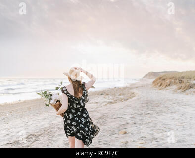 Junge Frau bei einem Spaziergang mit Blumenstrauß auf windigen Strand, Rückansicht, Menemsha, Martha's Vineyard, Massachusetts, USA Stockfoto