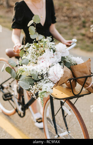 Junge Frau Fahrrad schieben mit Blumenstrauß auf den ländlichen Straßen-, Hals abwärts, Menemsha, Martha's Vineyard, Massachusetts, USA Stockfoto