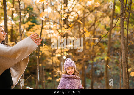 Mutter und Tochter werfen Blätter im Herbst in der Luft im Wald Stockfoto