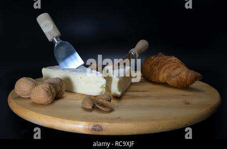 Holz- drehbare Platte mit französischem Käse genannt Brie mit einem Messer und einem französischen Croissant und Walnüsse und Mandeln Stockfoto