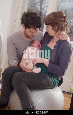 Junge Eltern halten ihre neugeborene Tochter im Arm, das Art ist 12 Tage alt und schreit | junge Eltern ihr neugeborenes Baby in ihren Armen halten - die Stockfoto