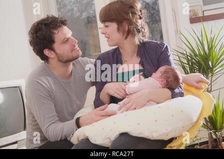 Junge Eltern halten ihre neugeborene Tochter im Arm, das Art ist 12 Tage alt | junge Eltern ihr neugeborenes Baby in ihren Armen halten - das Baby ist 12. Stockfoto