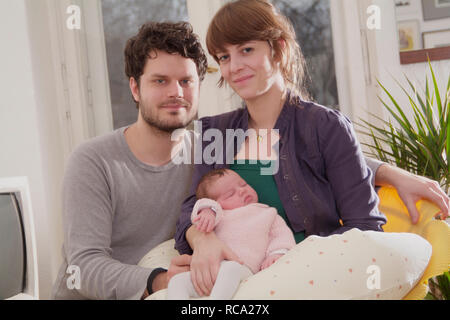 Junge Eltern halten ihre neugeborene Tochter im Arm, das Art ist 12 Tage alt | junge Eltern ihr neugeborenes Baby in ihren Armen halten - das Baby ist 12. Stockfoto