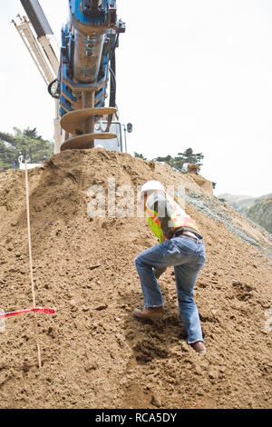 Männliche Bauarbeiter gehen auf einen großen Haufen von Schmutz vor einer Maschine auf einer Baustelle. Stockfoto