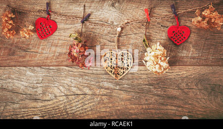 Blumen Komposition. Rahmen aus getrockneten Blüten Hortensie, handgefertigte Gestricken roten Herzen auf rustikalen Holzmöbeln Hintergrund.. Flach, Ansicht von oben, kopieren Raum Stockfoto