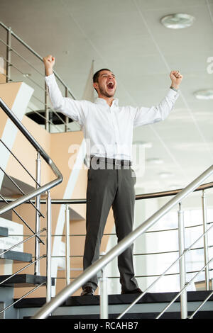 Erfolge feiern. Begeistert junge Unternehmer halten die Arme angehoben und das Ausdrücken von positivität beim Stehen in der Bürogebäude. Stockfoto