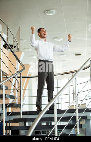 Erfolge feiern. Begeistert junge Unternehmer halten die Arme angehoben und das Ausdrücken von positivität beim Stehen in der Bürogebäude. Stockfoto