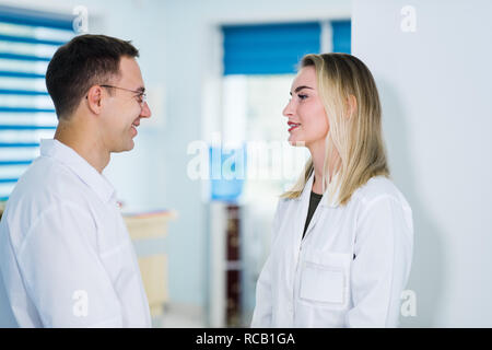 Hübscher junger Arzt spricht mit seiner schönen weiblichen Assistant, stehend im Warteraum der Klinik Stockfoto
