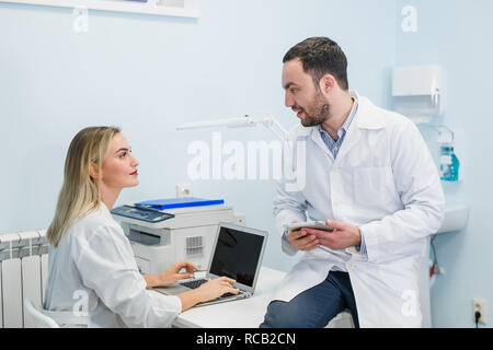 Zwei ärzte Kollegen sitzen am Arbeitsplatz und mit moderner Technologie für ihre Arbeit, in weißen Kitteln, fokussiert Stockfoto