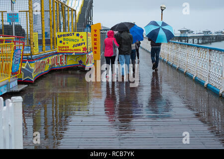 Menschen zu Fuß im Regen auf Llandudno Pier, Conwy, Wales, Großbritannien Stockfoto