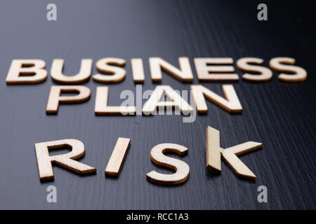 Die Inschrift ist von Buchstaben aus Holz auf dem Tisch cut angeordnet. Das Wort business plan, Risiko. Der dunkle Hintergrund. Stockfoto