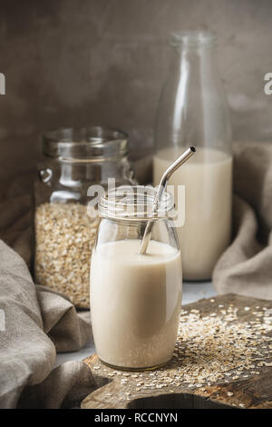 Nicht Molkerei Hafermilch in Glas Glas mit Metall wiederverwendbare Trinkhalm auf rustikalen Hintergrund. Haferflocken auf dem Tisch verteilt. Stockfoto