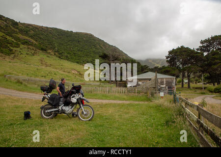 Flea Bay, Canterbury, Neuseeland - 6. Januar 2019: Ein Mann auf einem Motorrad nimmt einen Bruch am Ende der windigen Straße hinunter in die Bucht Stockfoto