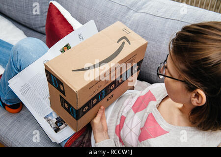 PARIS, Frankreich - Jan 6, 2018: die Frau auf dem Sofa lesen Zeitung und Vorbereiten der Unbox die Amazon Prime Paket Stockfoto