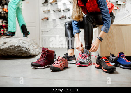 Frau, die versucht, verschiedene trail Schuhe für Wandern im Sportgeschäft, Nahaufnahme mit kein Gesicht Stockfoto