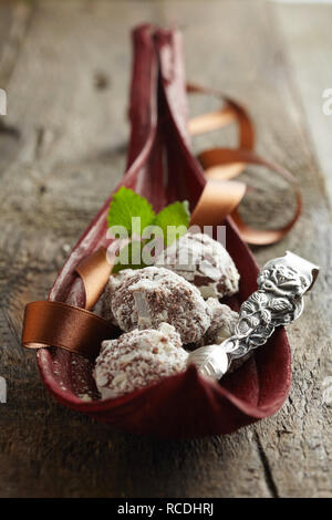 Gourmet handgemachte Schokolade Bonbons auf einem rustikalen Buffet in einem roten Blatt Deckblatt mit stilvollen silber Zangen angezeigt Stockfoto