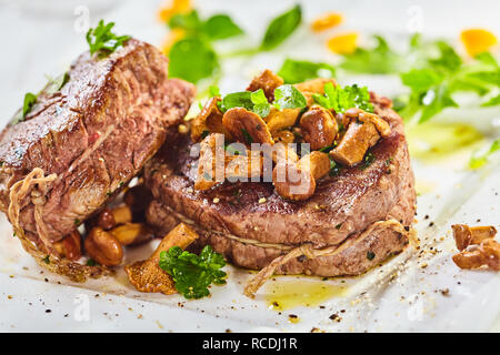 Seltene geröstete Dicken saftigen Rinderfilet Medaillon gekrönt mit geschmorten Pilzen und abgeschmeckt mit frischen Kräutern und Gewürzen in der Nähe zu sehen, für ein Menü oder Stockfoto