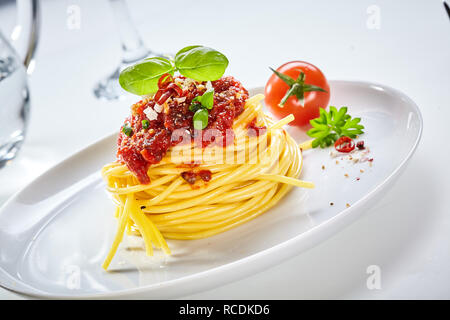 Spaghetti Bolognese mit Tomaten mit Parmesan und gewürzen bestreut und mit Basilikum mit einem frischen Tomaten auf einem geneigten whi serviert garniert Stockfoto
