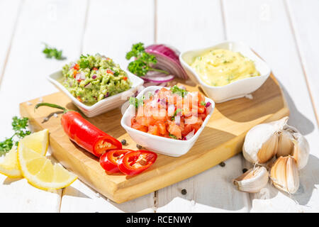 Auswahl an mexikanischen Soßen - Salsa, Guacamole, Käse Sauce und Zutaten, weiß Holz Hintergrund Stockfoto