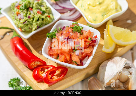 Auswahl an mexikanischen Soßen - Salsa, Guacamole, Käse Sauce und Zutaten, weiß Holz Hintergrund Stockfoto