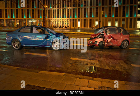 Zwei Autos Unfall. Abgestürzt Autos auf der Straße am Ort in der Stadt in der Nacht. Eine blaue sedan gegen eine rote Stadt Auto. Frontalcrash mit großen Schäden. Stockfoto