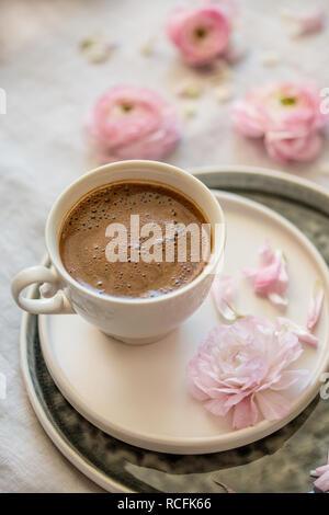 Feder Konzept. Eine Tasse schwarzer Kaffee mit rosa Ranunkeln um es. Vertikale Komposition. Stockfoto