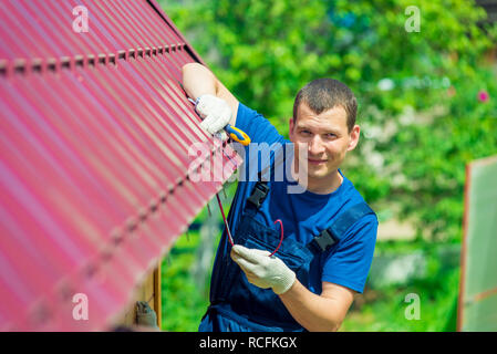 Ein junger Mann Reparaturen das Dach des Hauses in Overalls mit einem Werkzeug Stockfoto