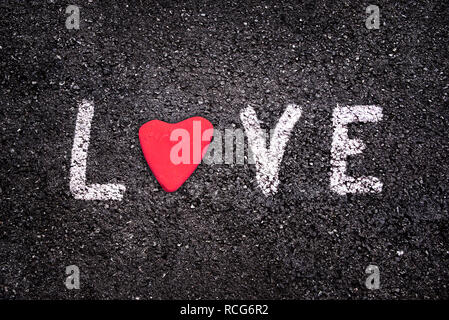 Valentines Tag Karte, Wort Liebe auf Asphalt Hintergrund mit einem roten Stein in der Form eines Herzens geschrieben Stockfoto