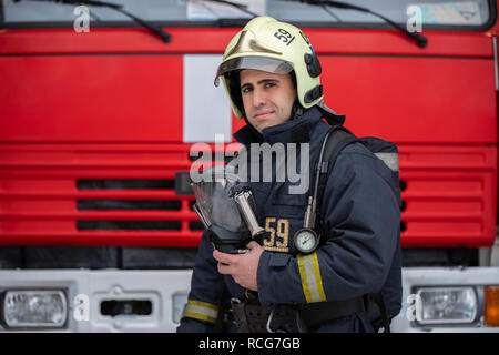 Foto von Mann Feuerwehrmann mit Maske in der Hand in der Nähe von Feuer Lkw Stockfoto