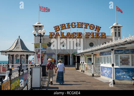 Ein paar walks​ Hand in Hand entlang Brighton Palace Pier an einem Sommertag. Stockfoto