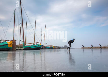 Die Niederlande, Sloten, Eislaufen. Hintergrund traditionelle cargo Segelboote. Winter. Stockfoto