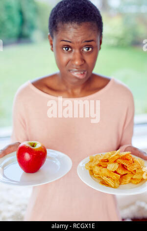 Ethnische Mädchen unentschlossen, ob Chips oder einen Apfel zu essen Stockfoto