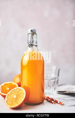 Flasche gesunde organische Orangensaft mit Orangen, Glas und Strohhalme auf weißem Marmortisch über rosa Hintergrund. Im Sommer trinken. Kopieren Sie Platz für Text. Stockfoto