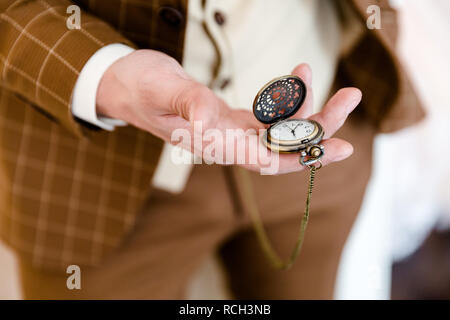 Ein Mann in einem braun-karierten Anzug hält in seiner Hand ein geöffnetes Taschenuhr, die sichtbar ist. Schließen Foto Stockfoto