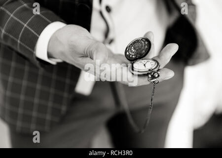 Ein Mann in einem karierten Anzug hält eine offene Taschenuhr in der Hand, das Zifferblatt wird sichtbar. Schwarze und weiße Nahaufnahme Foto Stockfoto