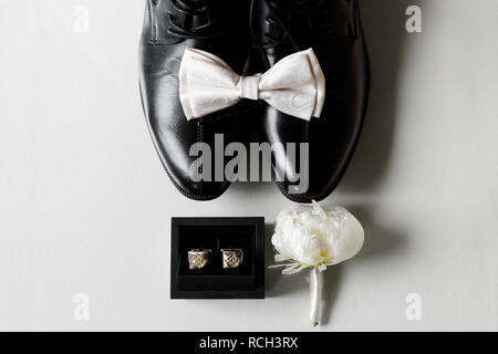 Foto eines weißen Bow Tie auf schwarze Schuhe, neben einer Box mit Manschettenknöpfe und Anstecker. Close-up auf einem weißen Hintergrund. Stockfoto