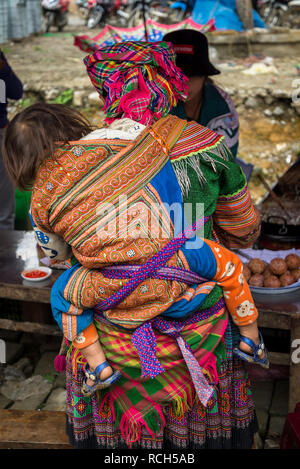 Baby auf dem Rücken der Mutter, bunte Bac Ha Markt am Sonntag in der Flower Hmong Minderheit Dorf im Norden von Vietnam Stockfoto