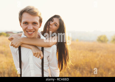 Sorglos Paar zusammen eine gute Zeit haben, genießen Liebe, Frische, Sonne und Natur, sie sind glücklich. Ein Kerl ein Mädchen auf seinem Rücken, in einem goldenen Stockfoto