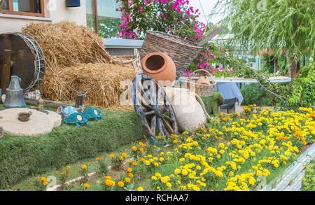 Garten Gestaltung und Dekoration. Antikes Holz Rad und Amphoren in den Garten. Dieser Garten hat Stroh und Bougainvillea. Retro Garten Innenbereich Stockfoto