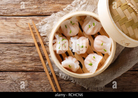 Hausgemachte Knödel dim sum mit ausgestopften Garnelen close-up in einem Bambus steamer Box auf dem Tisch. Horizontal oben Ansicht von oben Stockfoto