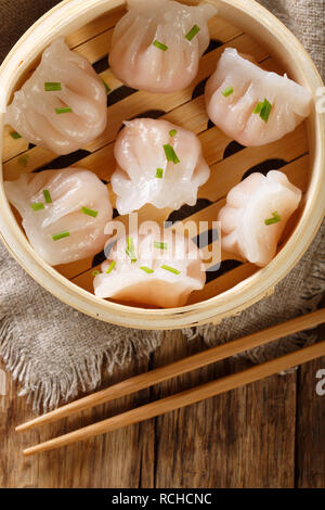 Hausgemachte Knödel dim sum mit ausgestopften Garnelen close-up in einem Bambus steamer Box auf dem Tisch. Vertikal oben Ansicht von oben Stockfoto