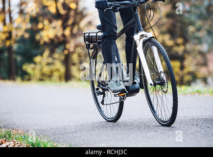 Eine nicht erkennbare Mann auf electrobike Radfahren im Freien auf einer Straße in Park. Stockfoto