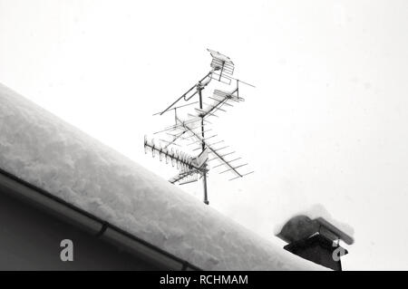 Schnee auf dem Dach nach zwei Tagen Schneefälle. Fernsehantenne mit Schnee bedeckt. Schwarz-weiß Foto. Schnee Zyklon in Europa Stockfoto