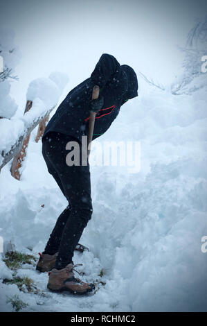 Mann mit Schneeschaufel reinigt die Bürgersteige im Winter. Winter. Zyklon in Europa Stockfoto