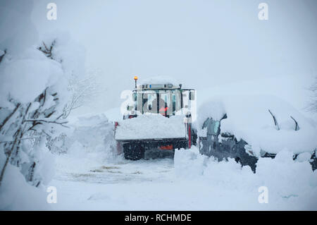 Winter service Traktor reinigen der Fahrbahn. Blick auf die Landschaft für einen Traktor, der Reinigung der Straße im Dorf. Ein Auto im Schnee gesperrt, nach einem Schnee c Stockfoto